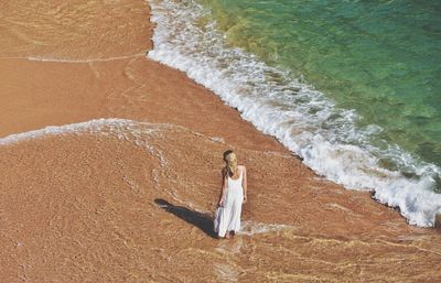 Rear view of woman standing in waves on shore at beach 