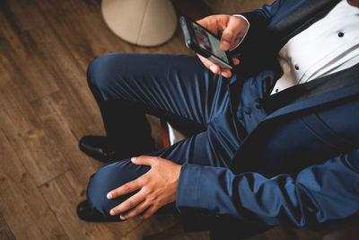 Low section of groom using phone while sitting on chair at home