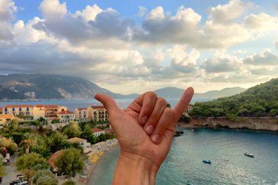 Person gesturing shaka sign by lake against sky