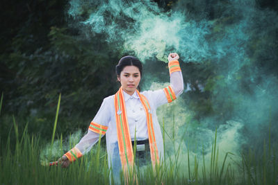 Portrait of woman holding distress flare while standing on field