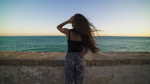 Woman standing at beach against sky during sunset