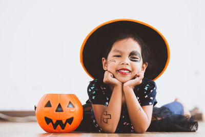 Portrait of cute playful girl with spooky make-up lying on floor at home during halloween