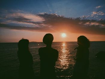 Silhouette people on beach against sky during sunset