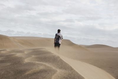 Rear view of man walking on sand dune at desert