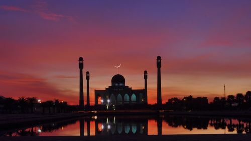 Silhouette mosque by lake against sky during sunset