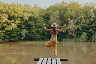 Side view of man with arms outstretched standing by lake