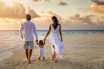 Rear view of family walking on beach against sky