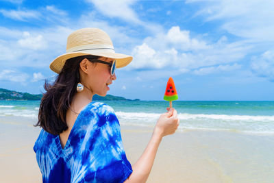 Woman holding popsicle at beach against sky
