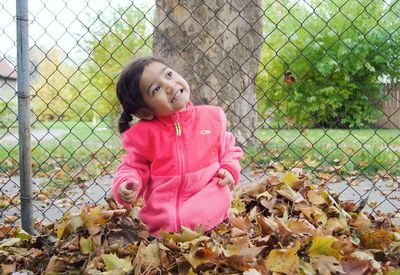 Girl looking away while standing by fence during autumn