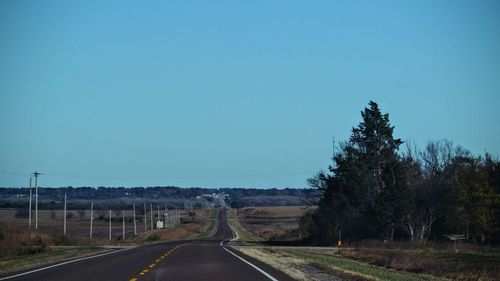 Road amidst trees against clear blue sky