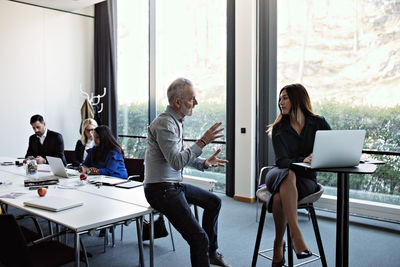 Senior businessman discussing to businesswoman using laptop with colleagues working at conference table in board room