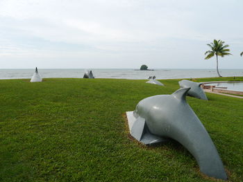 Dolphin sculptures on lawn by sea against sky