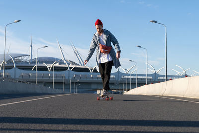 Man skateboarding on road against sky in city