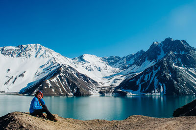 Full length of woman sitting by lake against mountains and sky