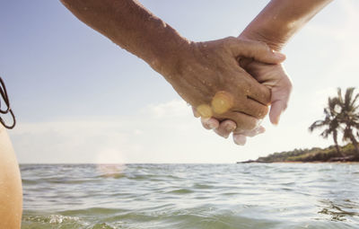 Cropped image of woman and girl holding hands at sea against sky