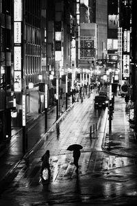 Wet walking on street amidst buildings in city at night