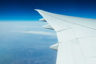 Airplane wing through window porthole, blue sky and white clouds, mood cold color toning
