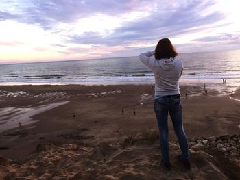 Rear view of woman standing on beach against sky