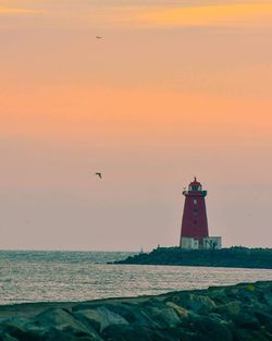 Lighthouse in sea at sunset