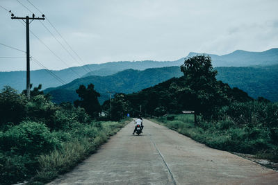 Rear view of man riding motorcycle on road against sky