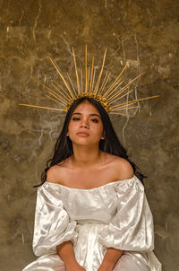 Portrait of teenage girl wearing crown against wall