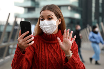 Woman wearing mask video calling on phone standing outdoors