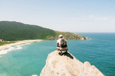 Man sitting on rock by sea against sky