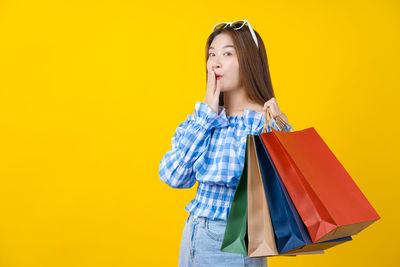 Young woman holding umbrella against yellow background