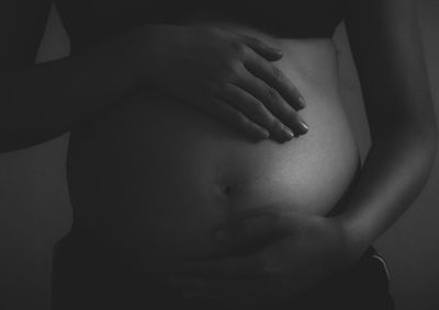 Midsection of woman touching hair over black background