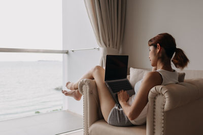 Young woman using phone while sitting on chair at home