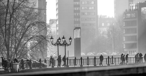 People walking on bridge in misty morning against buildings in city