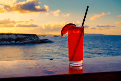 Red wine glass on beach against sunset sky