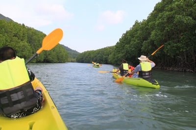 Rear view of people kayaking on river against sky