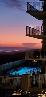 Modern building by sea against sky during sunset