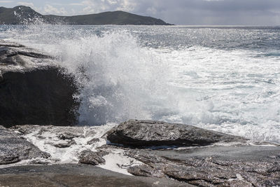 Waves splashing on rocks against sky