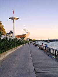 People on footpath by sea against clear sky