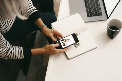 Senior woman taking photo of black and white photograph on book through mobile phone at home