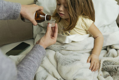 Female hands pour medicine for sick little girl