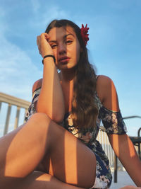 Low angle portrait of young woman sitting against blue sky