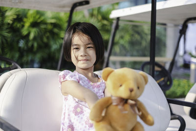 Smiling girl sitting with teddy bear on golf cart
