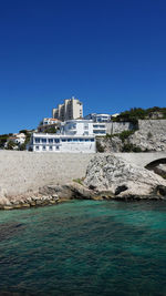 Buildings by sea against clear blue sky