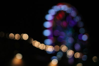 Defocused image of illuminated lights against sky at night