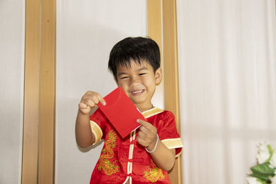 Happy boy holding red while standing against wall