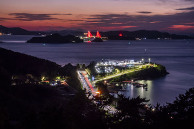 High angle view of the illuminated city by sea against the sky at sunset