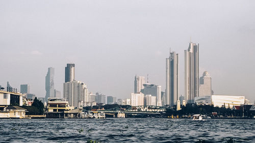 Sea by modern buildings in city against sky