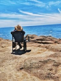 Rear view of man sitting on chair at beach