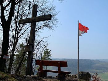 Red flag on bench by tree against sky