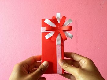 Cropped hands of woman holding gift box by pink wall