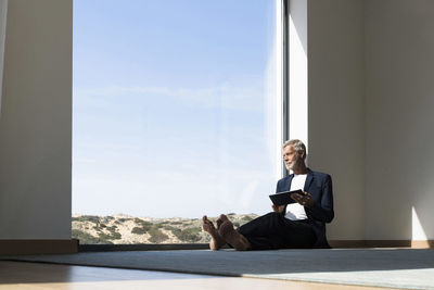 Senior businessman sitting at panorama window using tablet