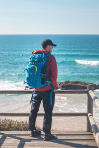 Rear view of man standing at beach against sky